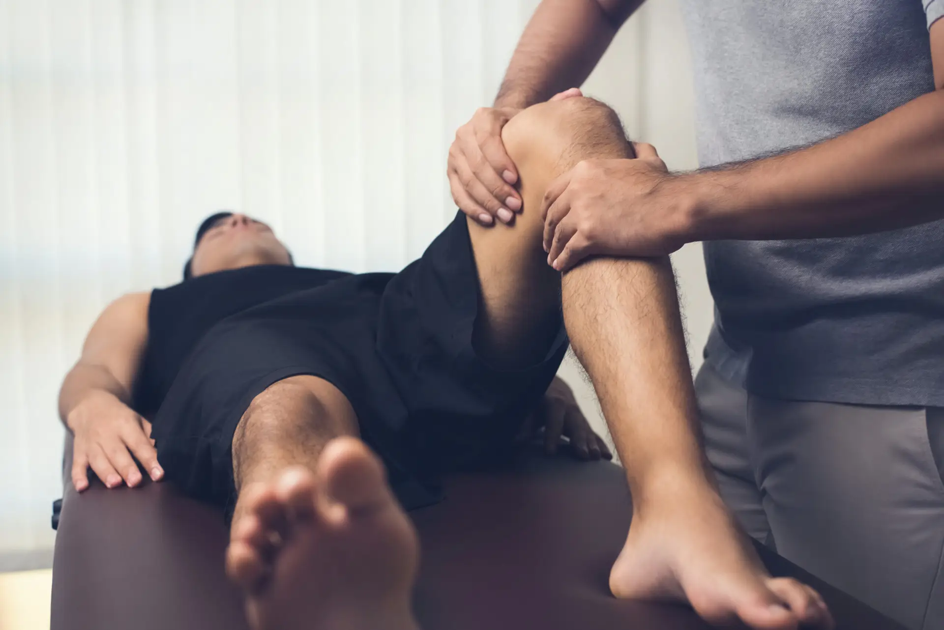 Mannelijke fysiotherapeut die de knie van een sportende patiënt behandelt – sportfysiotherapie concept.
